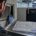 Entreprise 3d dératisation : technicien inspectant une grille murale en local technique